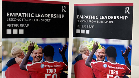 Four of Peter Sear's book displayed. the book cover is black and red with the image of two footballers in red kit hugging a man dressed in a suit and celebrating. The text reads'Empathetic Leadership: Lessons from Elite Sport' 'Peter Sear' 